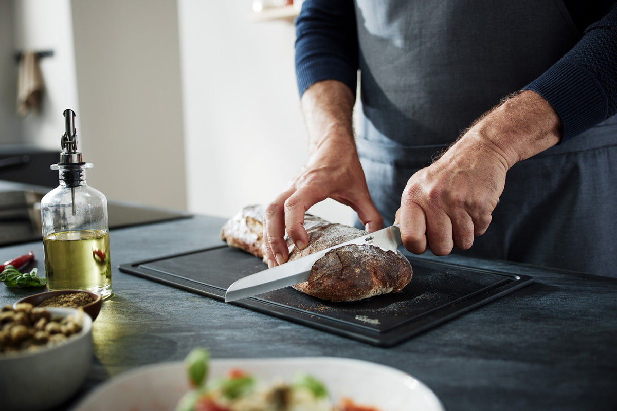 A person in an apron cuts bread on a board with the Fissler Essential® bread knife; Fissler cookware adds accents to the modern kitchen.