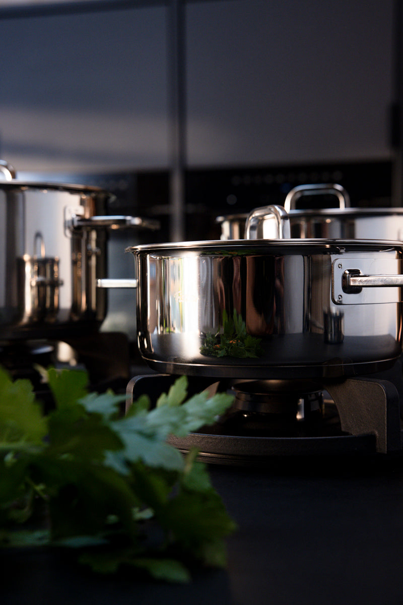 Fissler Viseo® Pro Bratentopf 20 cm mit Glasdeckel auf schwarzem Herd, der im Licht schimmert; frische Kräuter unterstreichen das zeitlose Design.