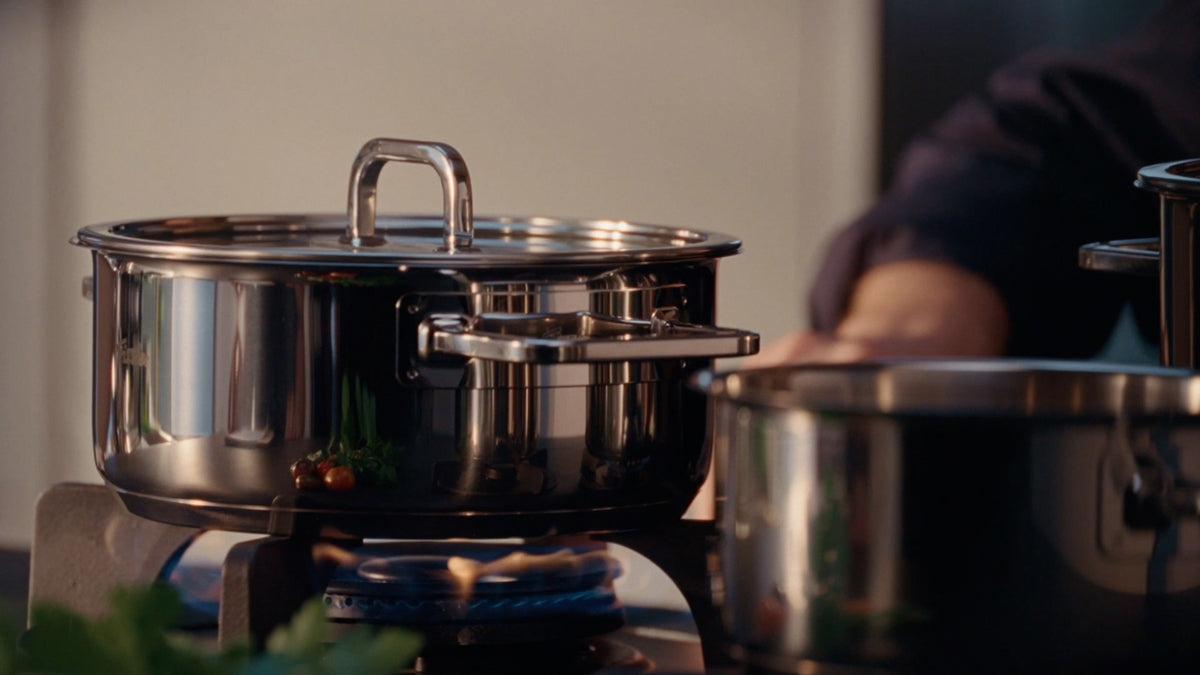 Fissler Viseo® Pro Casserole Pot 20 cm with Glass Lid on a gas stove, fresh herbs in the foreground. Modern top-class German Cookware.