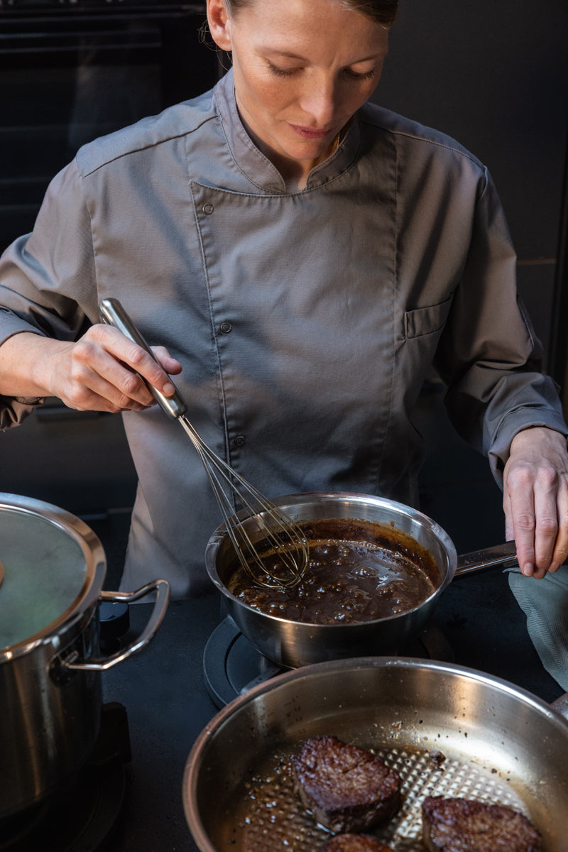 A chef uses the Fissler Original-Profi Collection® Cookware Set with Glass Lid for the sauce, while other Fissler pots and steaks sit beside it.