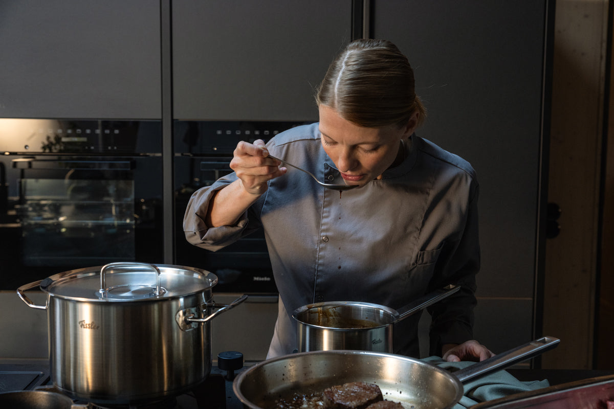 Ein Koch verkostet Speisen über einem 5-teiligen Set der Fissler Original-Profi Collection®, das die Qualität des deutschen Edelstahls auf dem Herd präsentiert.