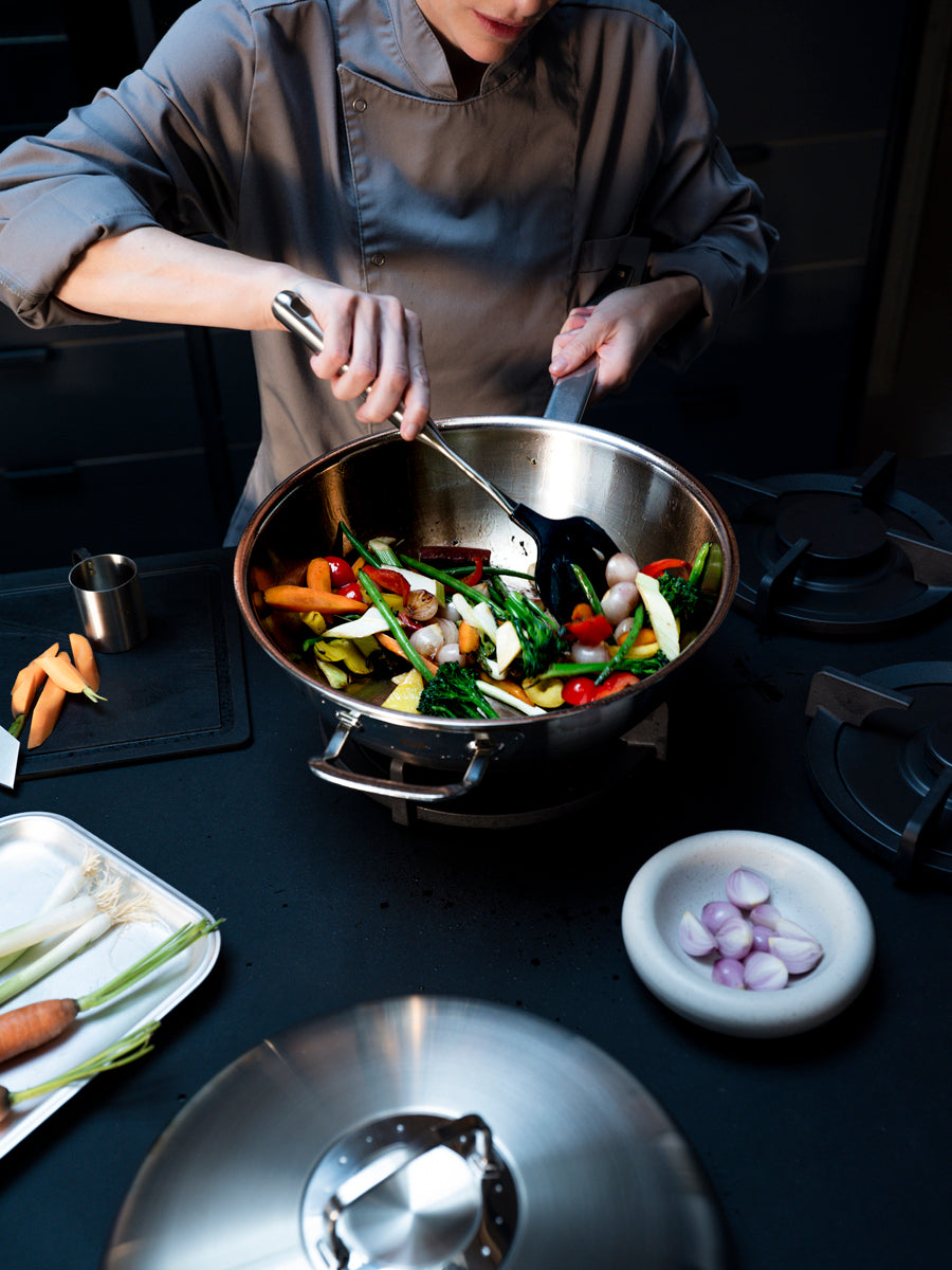 A chef stirs vegetables in the Fissler Original-Profi Collection® Wok 32cm, made in Germany with precision and timeless durability.