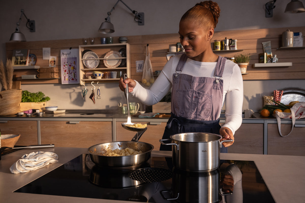 Eine Frau kocht in einer modernen Küche mit einem Fissler Pure Collection Kochtopf mit Glasdeckel - Präzisionsarbeit aus Deutschland - auf dem Herd.