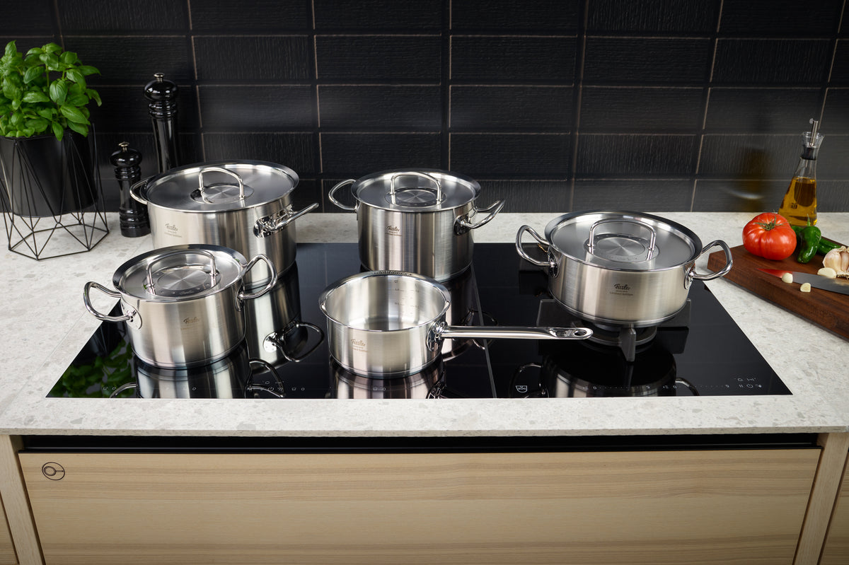 Fissler Original-Profi Collection® Retro 5-teiliges Edelstahlset auf dem Induktionsherd, mit frischen Zutaten und Utensilien in der Nähe.