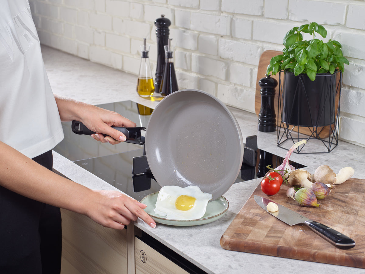 A person serves a fried egg from the Fissler Ceratal® Frying Pan Set - precision-made, durable pans - in a modern kitchen.