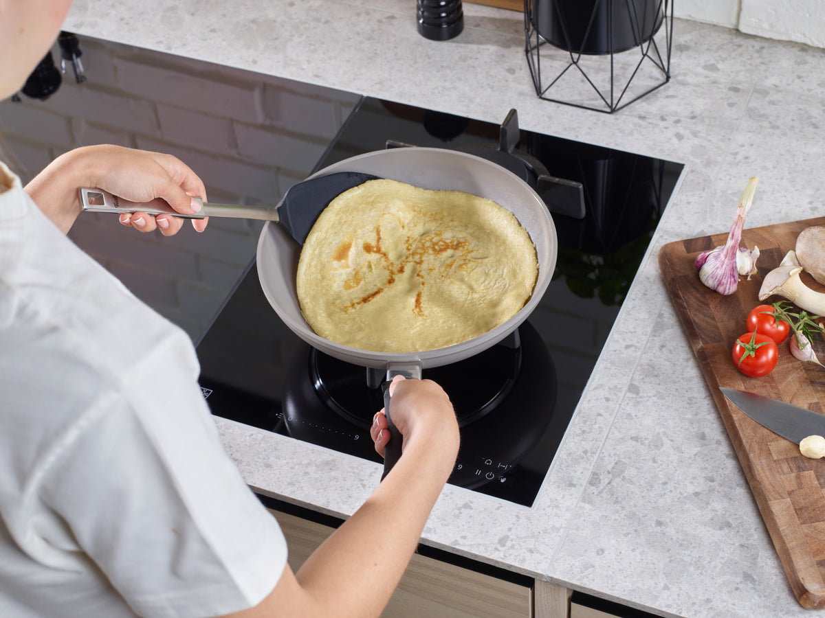 Preparing a pancake in a Fissler Frying Pan with the Original-Profi Collection® spatula; fresh produce sits beside it on a cutting board.