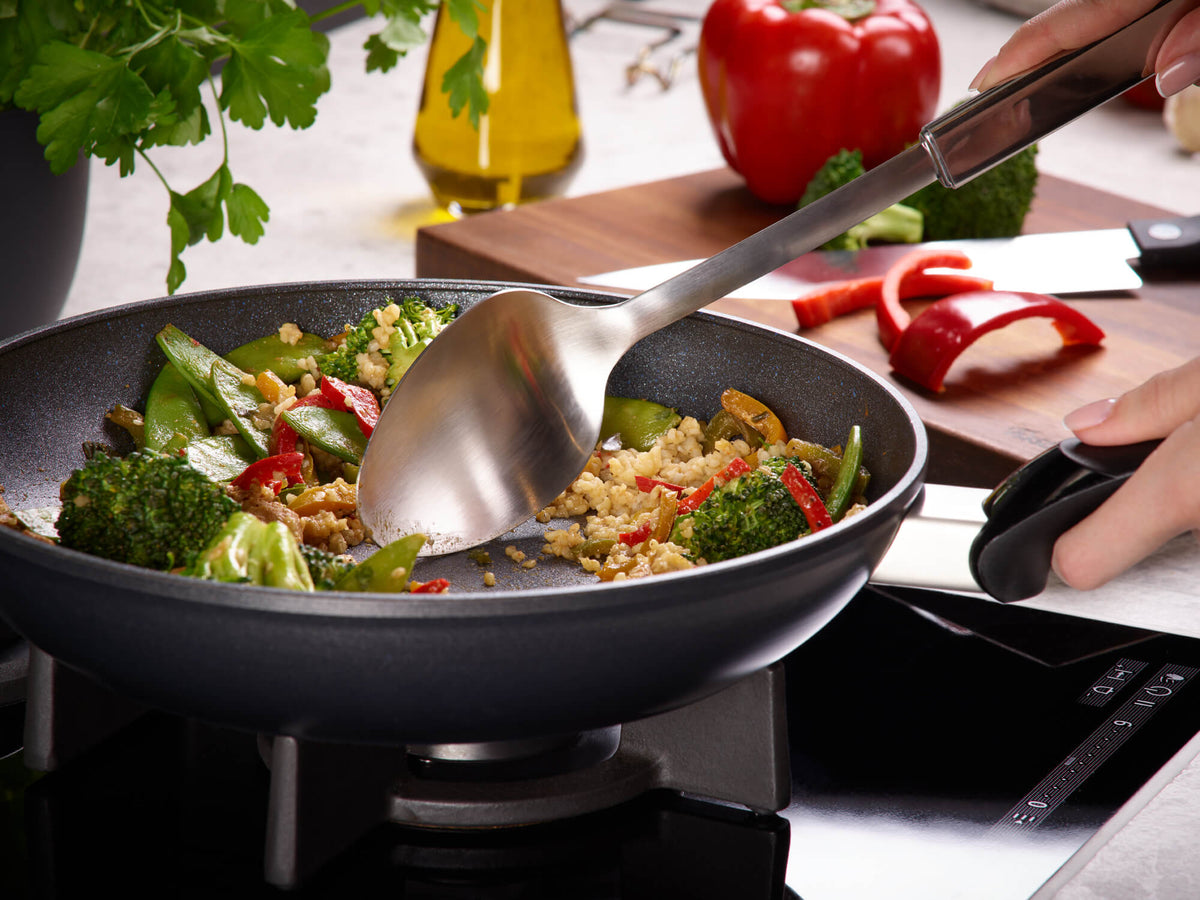 Gebratenes Gemüse und Reis in Fissler Adamant® Classic Pfannen mit Antihaftbeschichtung, hergestellt in Deutschland; dazu frische Kräuter und Paprika.