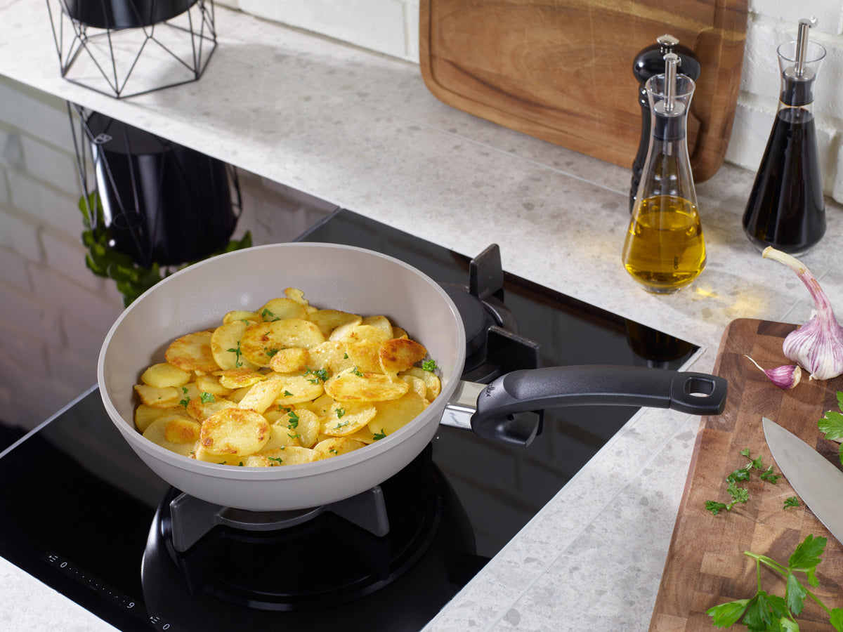 Golden potatoes cooking in Fissler Ceratal® Comfort PFAS/PTFE-free pans, 24 & 28 cm. German quality since 1845. Kitchen preparation shown.