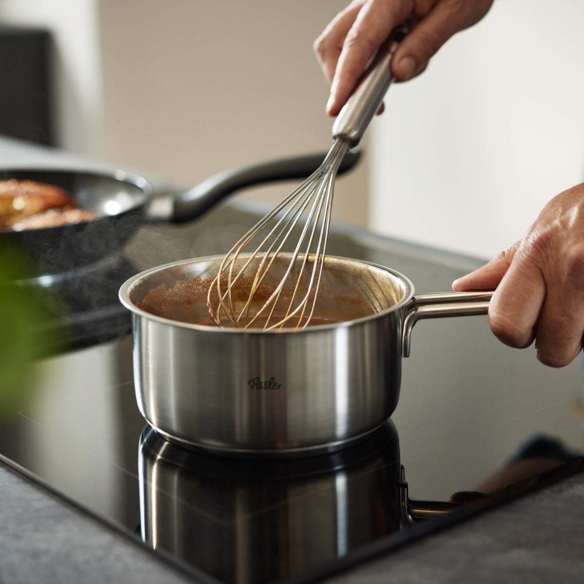 Verquirlen einer Sauce mit einem Fissler Essential® Becherbesen in einem Fissler Edelstahltopf, der zeitloses deutsches Design präsentiert.