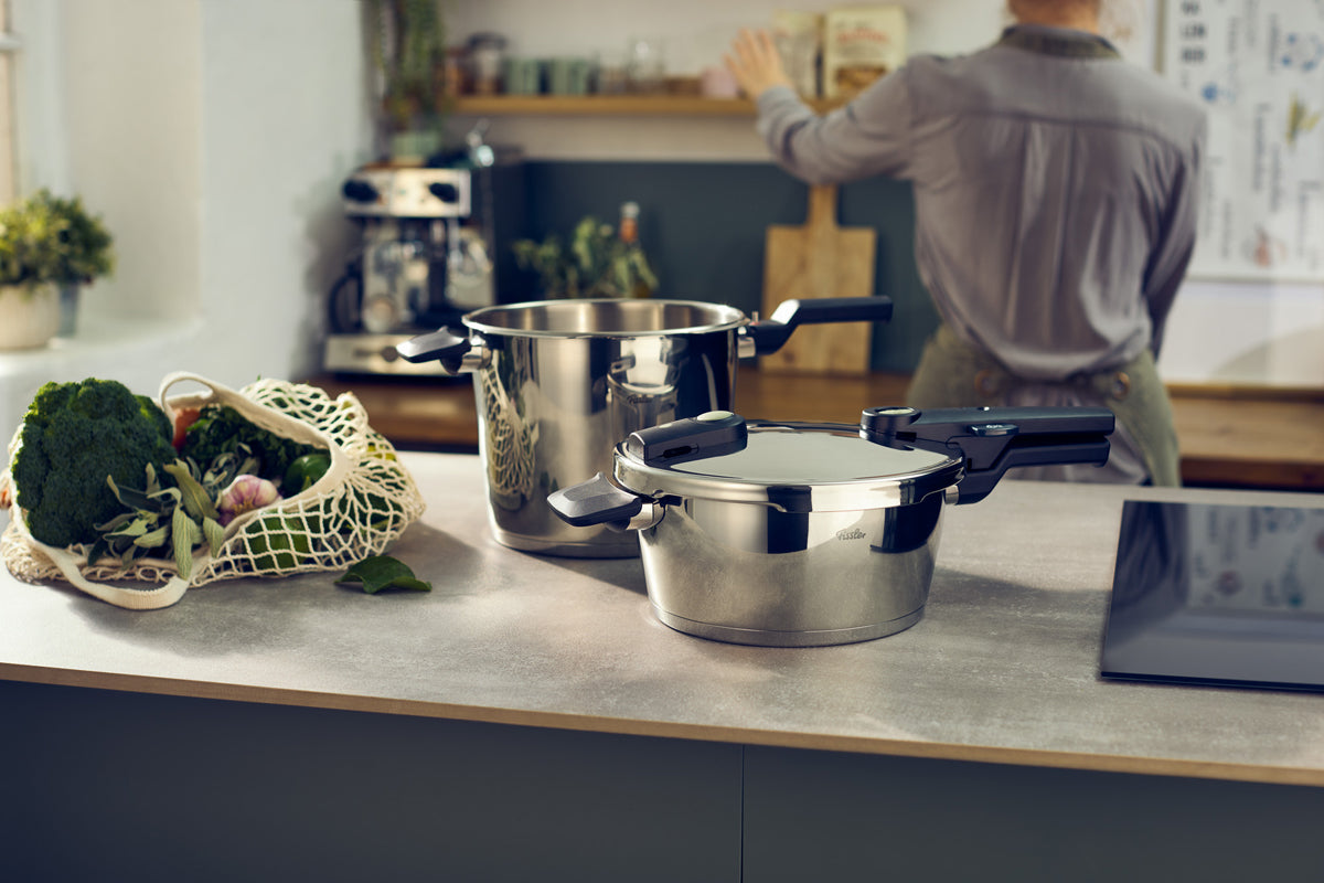 Fissler Vitaquick® Elemental 3-pc. pressure cooker set on counter, stainless steel design next to fresh produce.