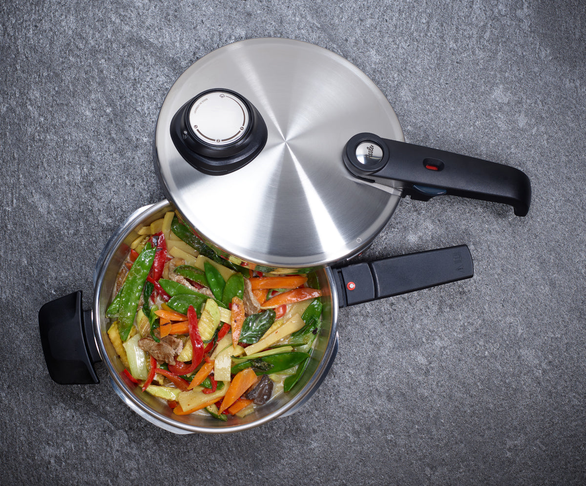 Die Fissler Vitavit® Premium Schnellbratpfanne aus hochwertigem Edelstahl 18/10, ausgestattet mit ergonomisch geformtem schwarzem Griff, ist teilweise geöffnet und präsentiert farbenfrohe gebratene Gemüsestreifen sowie zartes Rindfleisch – ein Beispiel für präzises Kochen auf einer edlen, grauen strukturierten Oberfläche. Die Innovation und das zeitlose Design von Fissler unterstreichen die Qualität „Made in Germany“.