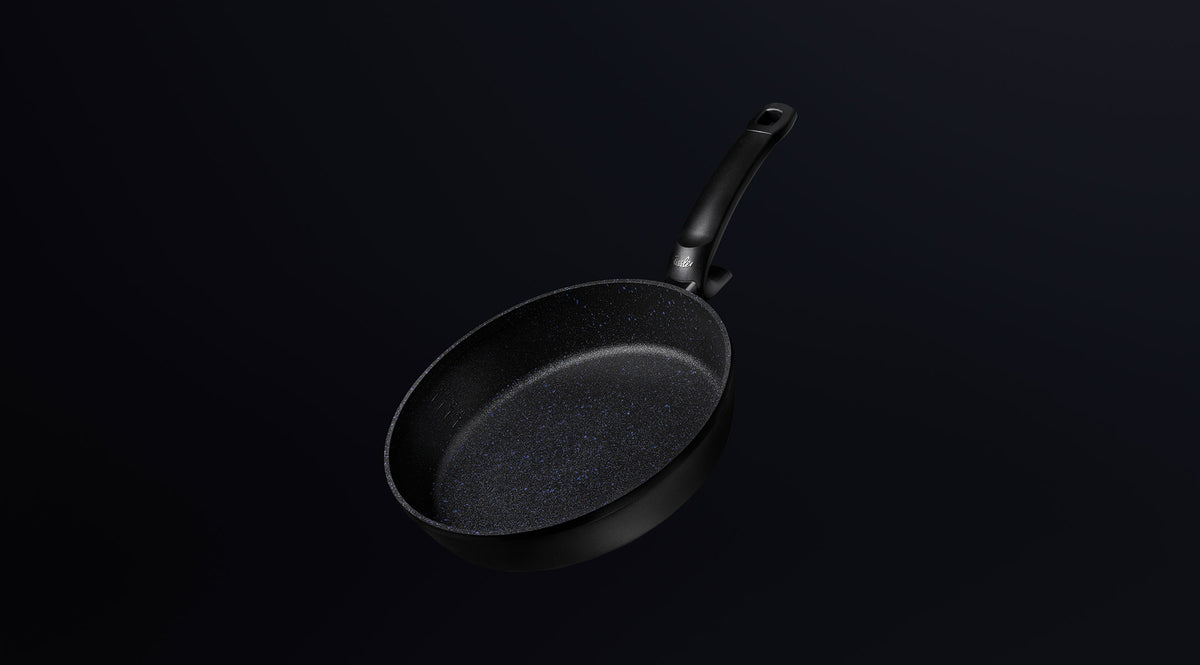 Eine schwarze, antihaftbeschichtete Bratpfanne von Fissler mit einem ergonomischen, langen Griff, der auf einem dunklen Hintergrund mit Farbverlauf angebracht ist, zeugt von deutscher Präzision.