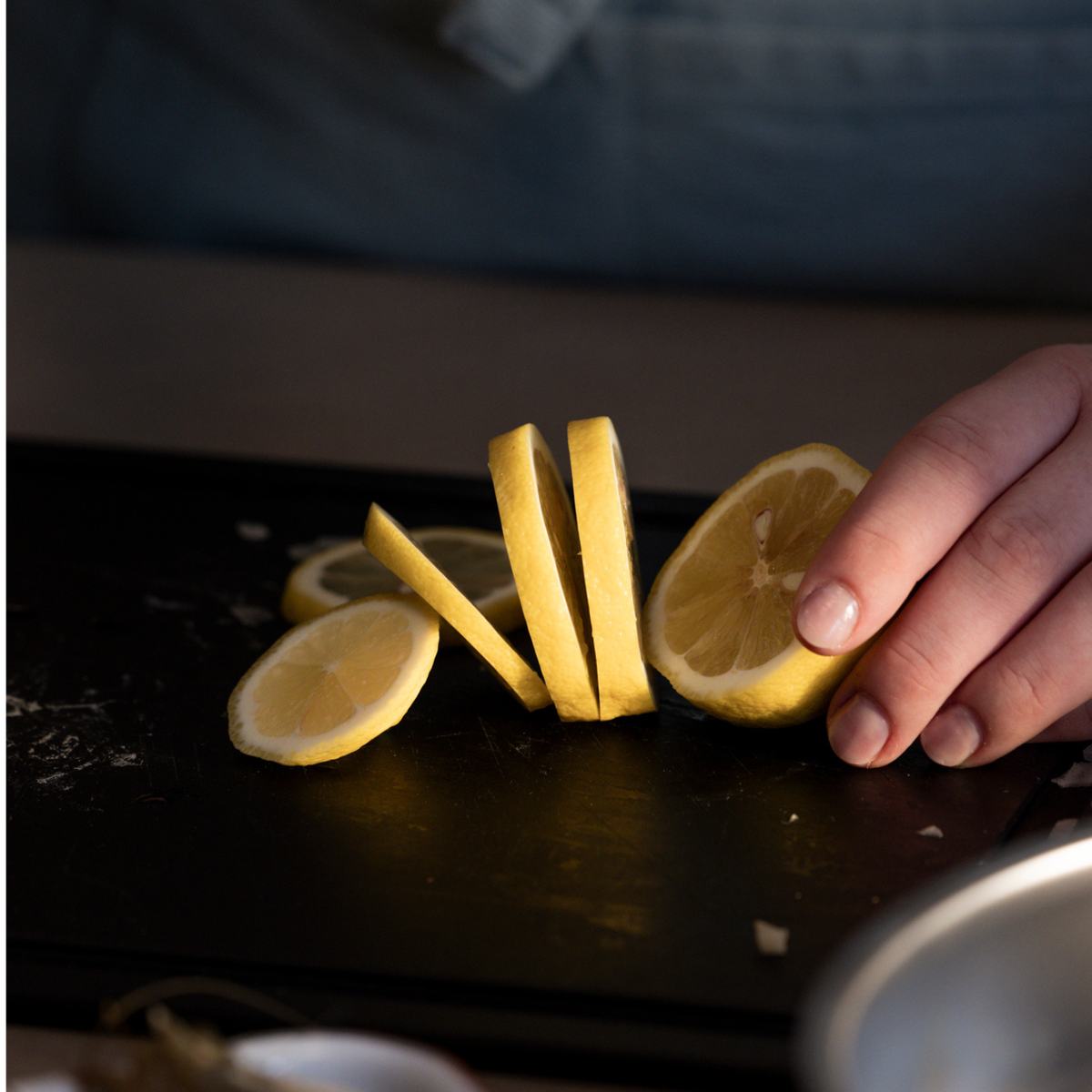 Eine geschickte Hand schneidet eine Zitrone auf einem eleganten schwarzen Fissler-Schneidebrett und demonstriert dabei Präzision und Kontrolle. Auf dem Brett liegen mehrere frische Zitronenscheiben, die das Engagement der Marke für hochwertiges Küchenzubehör widerspiegeln, das auf Langlebigkeit und zeitlose Eleganz ausgelegt ist.