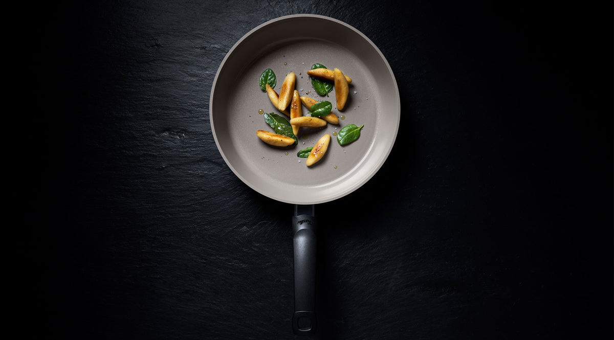 Fissler Antihaft-Pfanne auf dunkler Oberfläche mit goldbraunen Gnocchi und Basilikum, die von deutscher Präzision und zeitlosem Design zeugt.