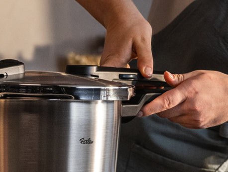 Hands secure the lid of the Fissler Vitaquick® Premium pressure cooker set, made in Germany for safe and fast cooking.