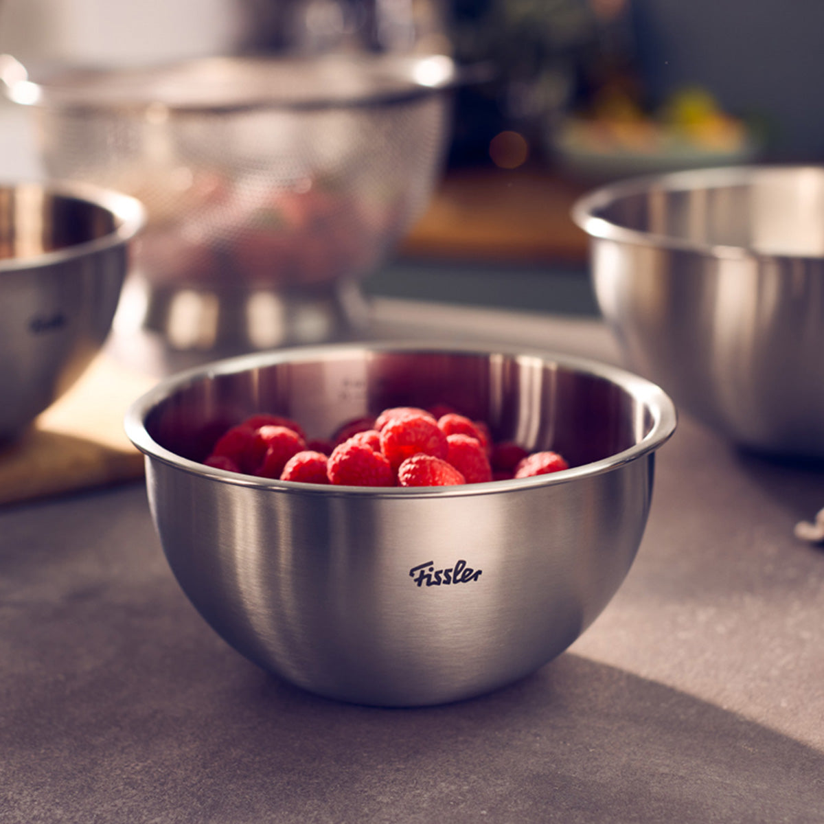 Fissler Essential® 16cm stainless steel bowl filled with raspberries, on the countertop next to other bowls.