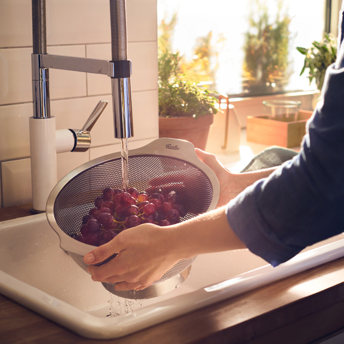 Red grapes, washed in a Fissler Essential® 24cm colander, sunlight through the window - German precision design for fresh, clean fruit.