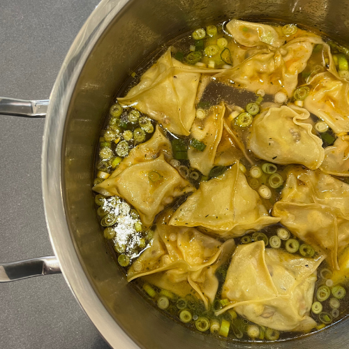 Wontons simmer in broth in a Fissler stainless steel pot, garnished with green onions - precision, durability, and innovation.