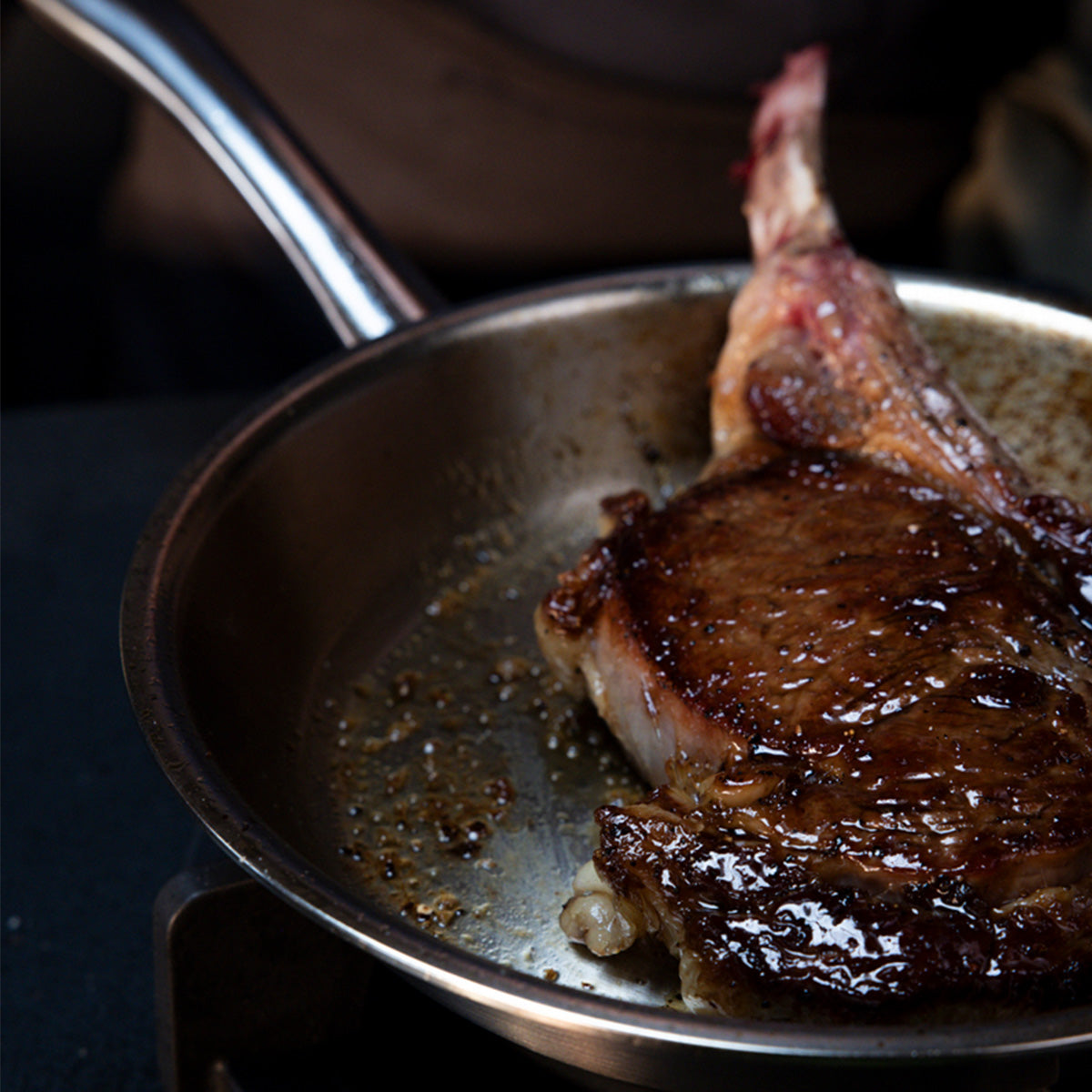A bone-in steak with a rich brown crust and succulent juices sears to perfection in the Fissler M5 Pro-Ply® 3-tlg. Set mit Metalldeckel, showcased on an induction-ready stovetop. The image highlights Fissler’s signature precision engineering and timeless German design, demonstrating durable performance for exceptional cooking results.