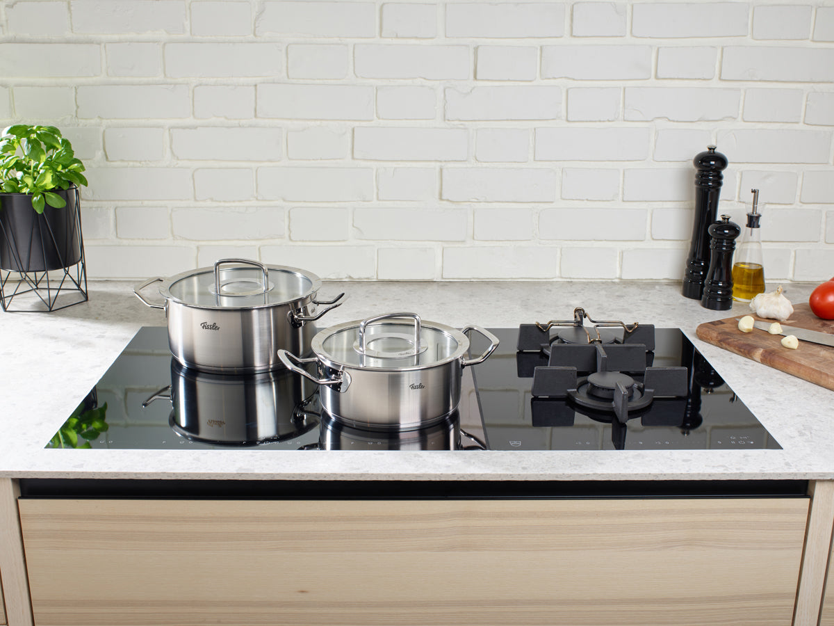 A modern kitchen with two Fissler Original-Profi Collection® Casserole Pots with Glass Lids on an elegant black glass cooktop.