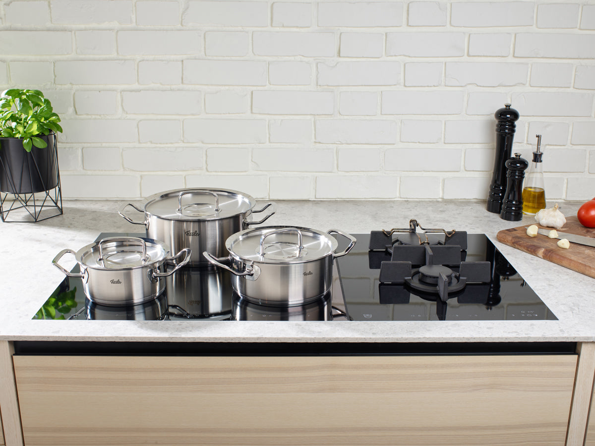 Drei Fissler Original-Profi Collection® Bratentöpfe auf einem Induktionsherd in einer schlichten Küche, die deutsche Präzision und Design verkörpert.