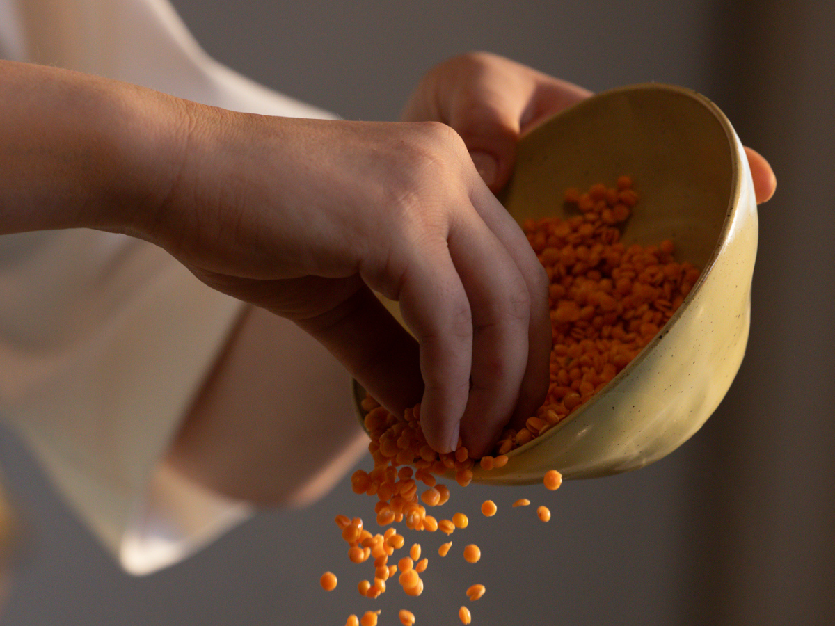 Eine Hand schüttet leuchtend orangefarbene Linsen aus einer sanft geschwungenen, hellbraunen Schüssel, wobei die Körner anmutig durch die Luft schweben. Diese Szene spiegelt Fisslers Engagement für hochwertige Küchenartikel wider – zeitloses Design und Präzision für müheloses Kochen.