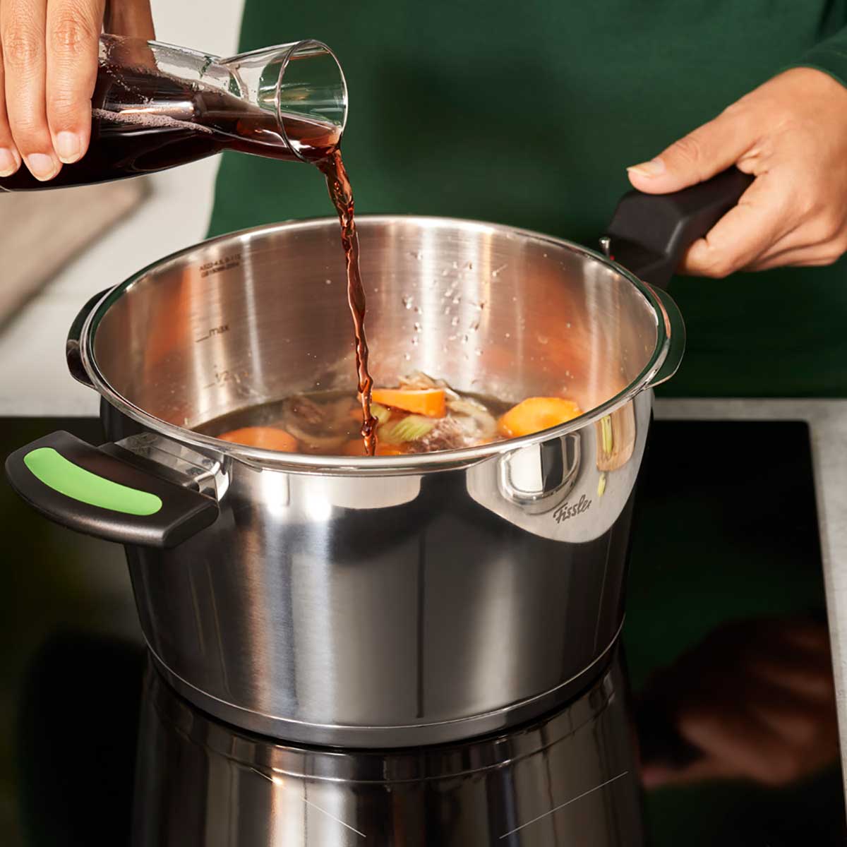 Eine Hand gießt eine dunkle Flüssigkeit in Gemüse, das im Fissler Vitaquick® Green Schnellkochtopf für gesundes Kochen köchelt.