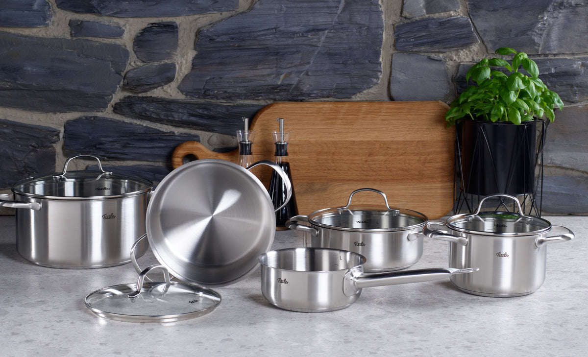 Erleben Sie außergewöhnliche deutsche Handwerkskunst mit dem Fissler San Francisco Schmortopf-Set: hochwertige Töpfe und Pfannen aus Edelstahl mit Deckeln, elegant auf einer Küchenarbeitsplatte arrangiert. Jedes Teil verfügt über unseren charakteristischen Superthermic-Boden für eine präzise, gleichmäßige Wärmeverteilung auf allen Herdarten – einschließlich Induktion. Ergänzt wird das Set durch ein Holzschneidebrett, zwei Ölflaschen und eine Basilikumpflanze im Topf, die das zeitlose Küchenbild
