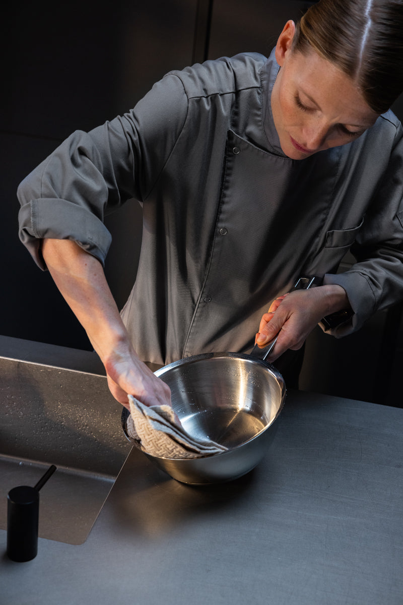 Ein Chefkoch in Grau poliert eine Fissler Original-Profi Collection® 20cm Sauteuse, die deutsche Präzision und zeitloses Design demonstriert.