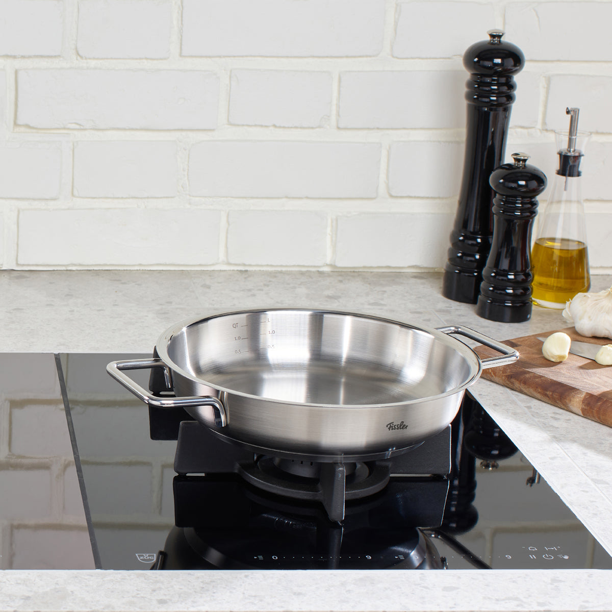 Eine in Deutschland gefertigte Fissler Pure Servierpfanne steht auf einem Gasherd in einer modernen Küche mit hochwertigen Kochutensilien in der Nähe.