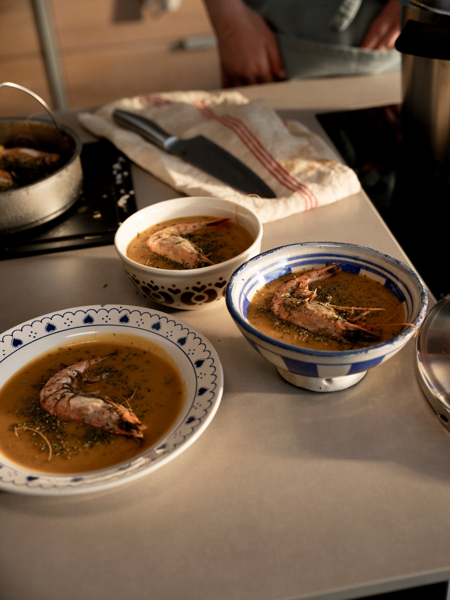 Drei Schalen mit Krabbensuppe auf einer Küchentheke mit Fissler-Topf und Messer, die deutsche Qualität und zeitloses Design ausstrahlen. Warme Beleuchtung.
