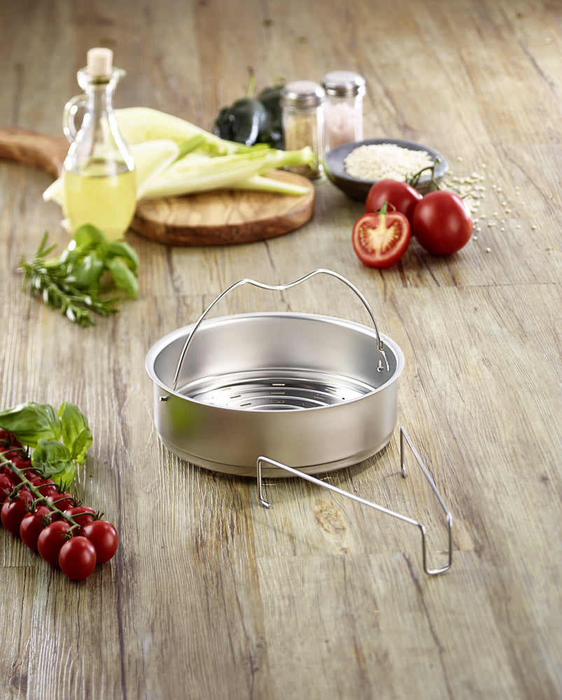 Fissler Schnellkochtopf-Zubehör Einsatz gelocht mit Griffen und Dreibein, umgeben von frischem Gemüse-modernem, funktionalem Design.