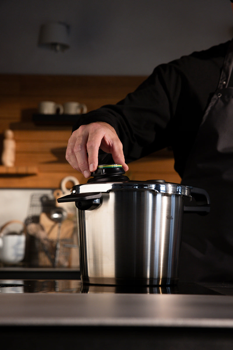 A chef attaches the lid of a Fissler Vitavit® Premium set - a German-made stainless steel pressure cooker - on a modern kitchen counter.