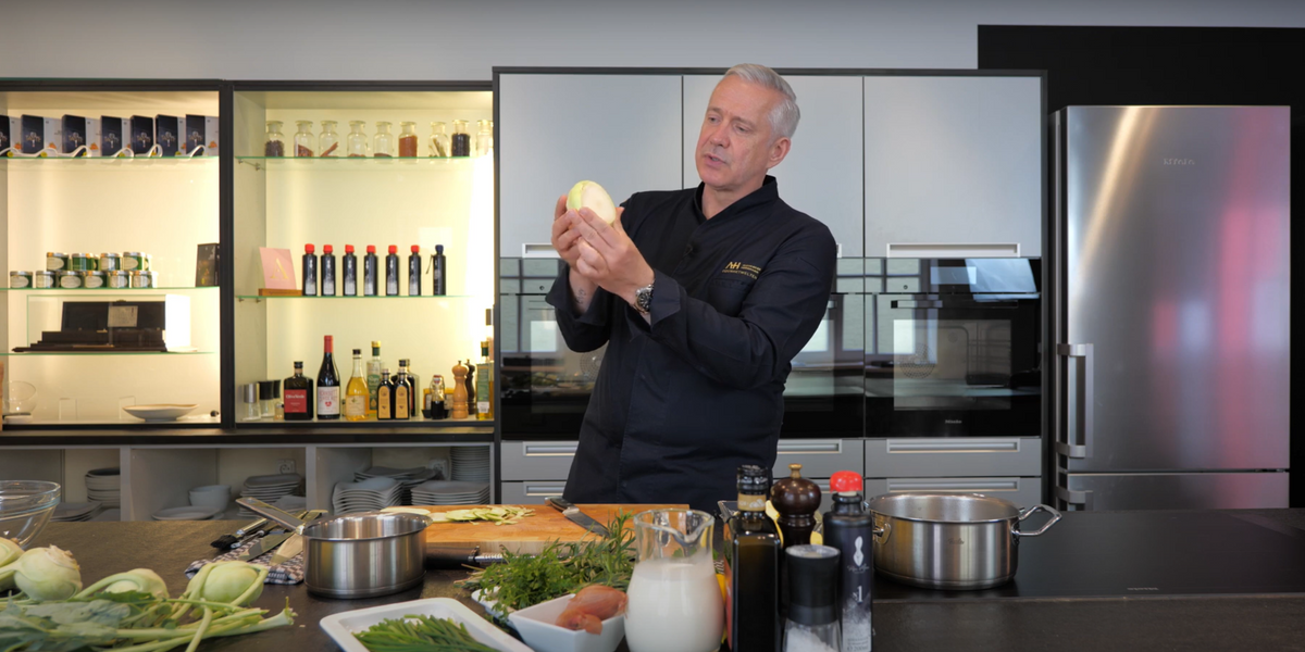 Ein Mann in einer modernen Küche prüft Fenchel, umgeben von Kräutern und Fissler-Edelstahlgeschirr auf der Arbeitsplatte.