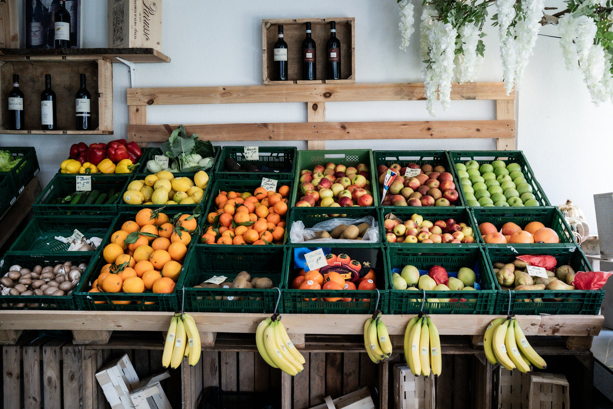 Eine lebendige Marktauslage mit frischem Obst und Gemüse, die in Körben neben Weinflaschen angeordnet ist - perfekt für Fissler-Kochgeschirr.