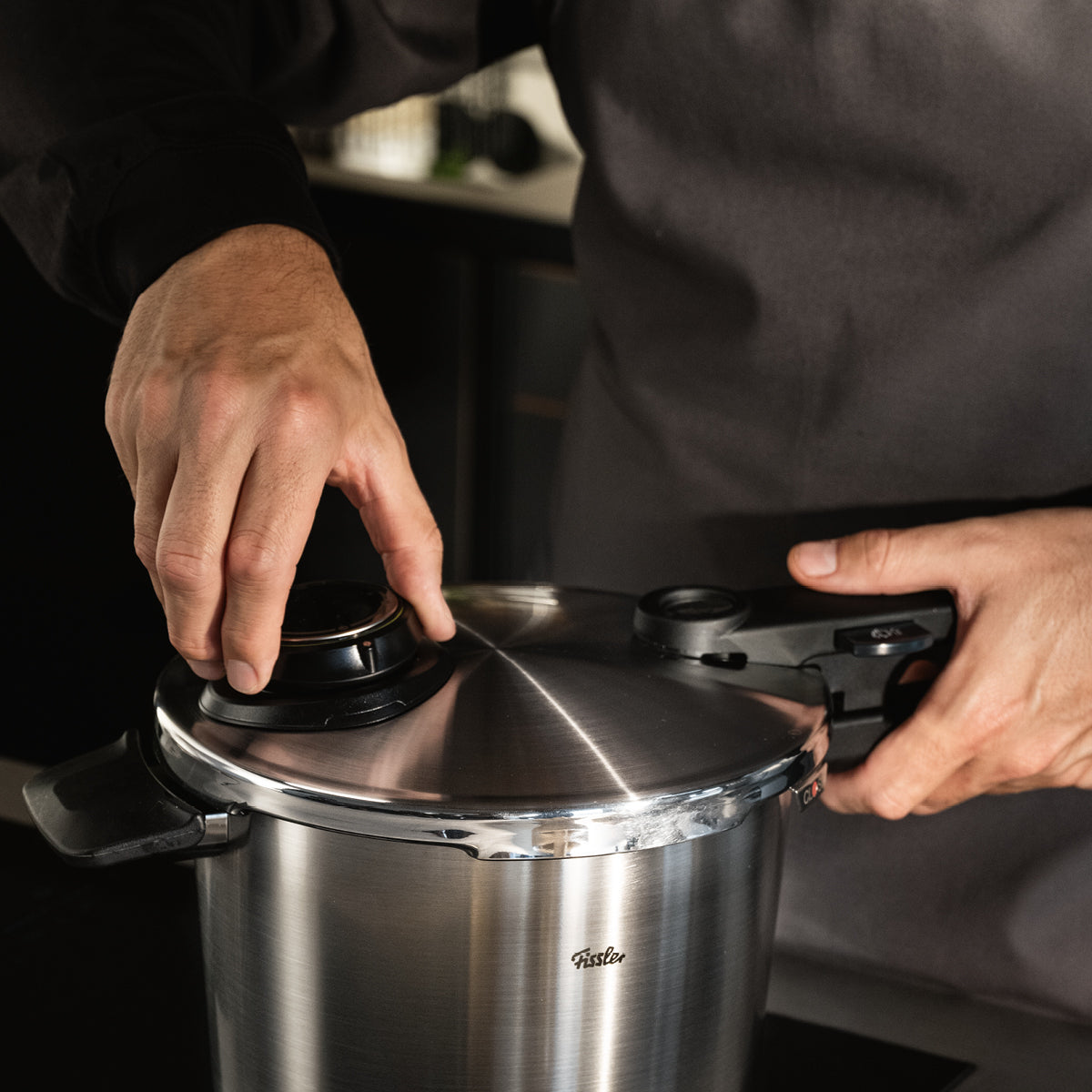 Eine Person befestigt den Deckel eines Fissler Schnellkochtopfes aus Edelstahl auf einem Küchentisch, der deutsche Präzision und Design demonstriert.