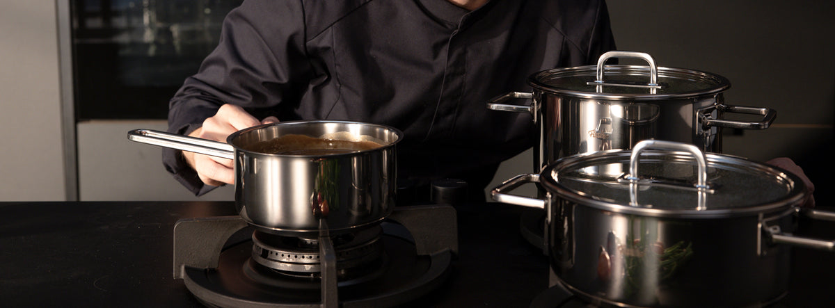 Ein Koch rührt Speisen in Fissler-Edelstahltöpfen auf einem Gasherd in einer modernen Küche, die deutsche Präzision und Design widerspiegelt.