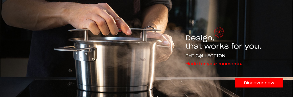 A person lifts the lid from a steaming Fissler stainless steel pot on a stovetop, showcasing precision engineering and timeless German design. Text reads: Design, that works for you. PHI COLLECTION. Made for your moments. A red button invites: Discover now.