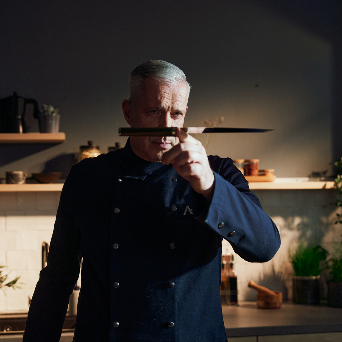A chef in a modern kitchen inspects a Fissler knife, a premium cookware item known for German precision and timeless design.