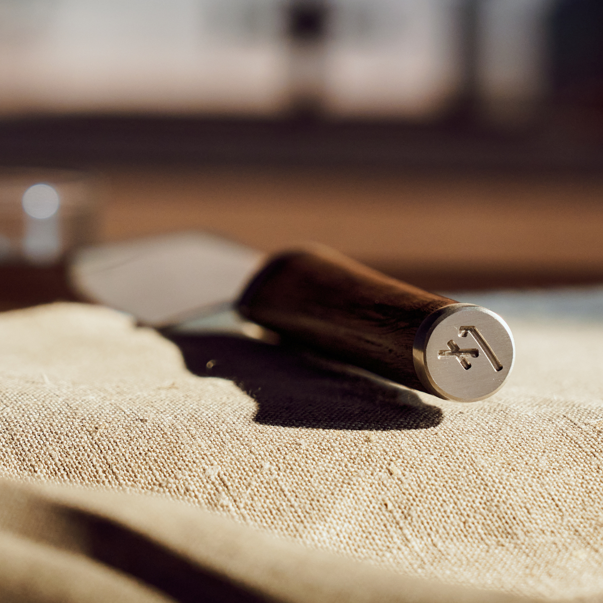 Close-up of a Fissler kitchen knife with a wooden handle and engraved logo, resting on beige fabric, made in Germany.