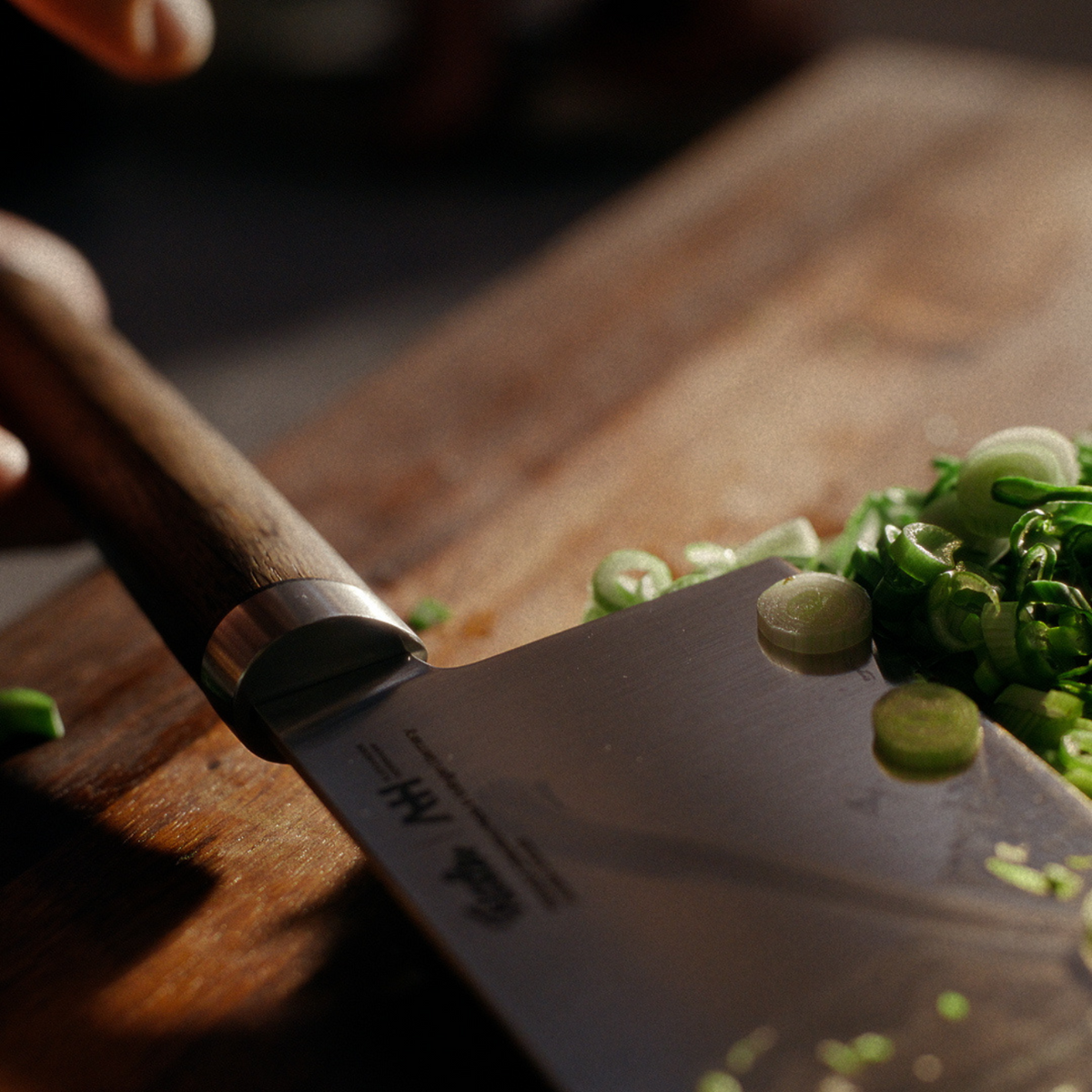 A precisely crafted Fissler chef's knife slices green onions on a wooden cutting board, with sunlight illuminating every fresh detail.