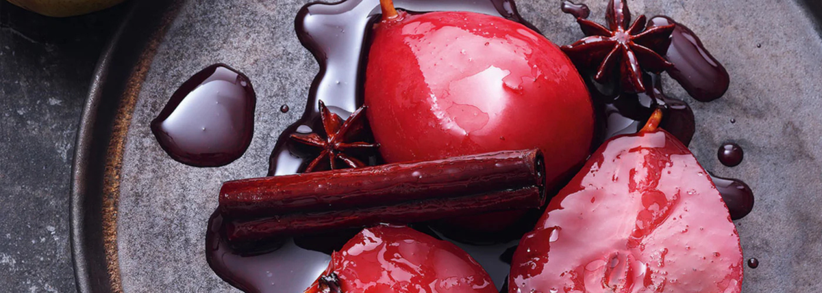 Three poached pears in red wine with star anise and cinnamon, served on a dark plate, refined with rich syrup - precisely arranged.