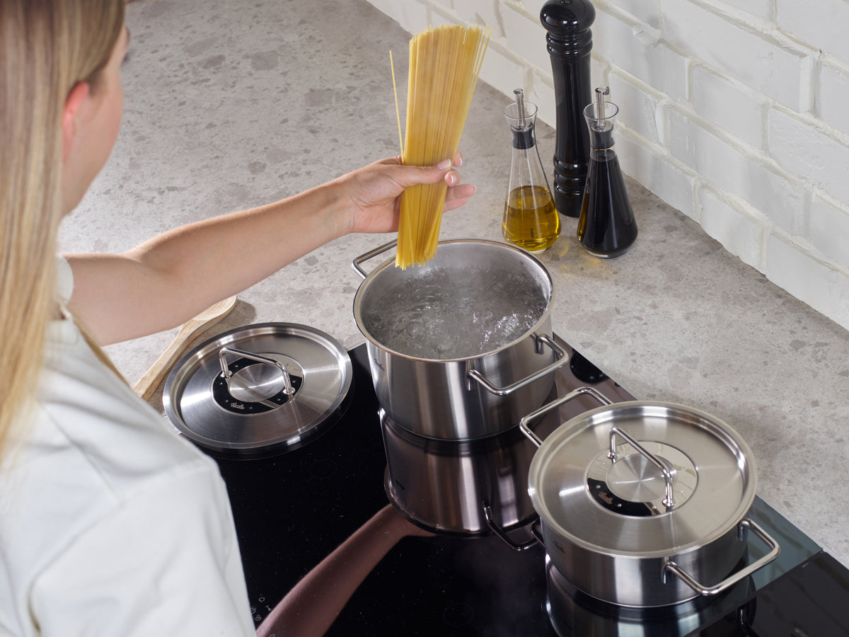 Eine Person kocht Spaghetti über kochendem Wasser mit zwei Fissler Pure Collection Kochtöpfen mit Metalldeckel auf dem Tresen, die in Präzisionsarbeit hergestellt wurden.