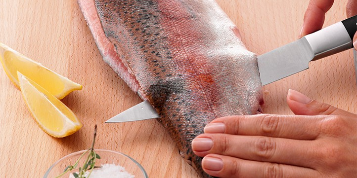 Ein präzises Messer schneidet das Fischfilet auf einem Holzbrett, daneben liegen Zitronenscheiben und Salz - ein Beweis für Fisslers Kücheninnovation.