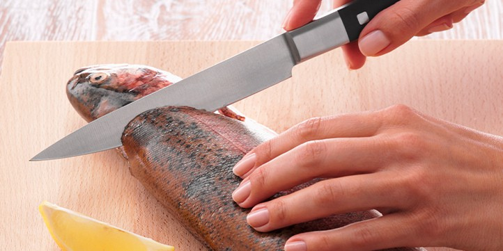 Ein Koch filetiert fachmännisch einen Fisch auf einem Holzbrett mit einem Fissler-Präzisionsmesser; daneben Fissler-Kochgeschirr und eine Zitronenspalte.