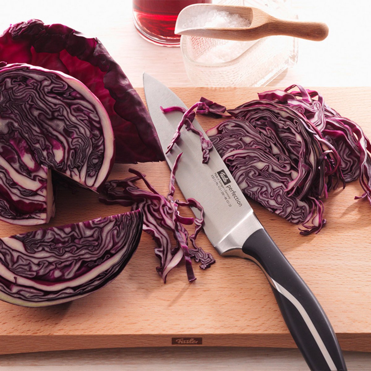 Ein Fissler-Kochmesser auf einem Holzbrett mit geschnittenem violettem Kraut, das deutsche Präzision und zeitloses Küchendesign demonstriert.