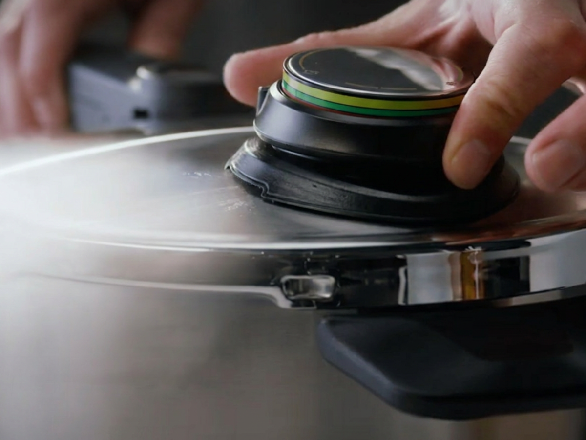 Eine Nahaufnahme einer Hand, die das Druckventil am Deckel eines Fissler-Edelstahl-Schnellkochtopfs präzise einstellt – ein Beispiel für deutsche Ingenieurskunst und zeitloses Design.