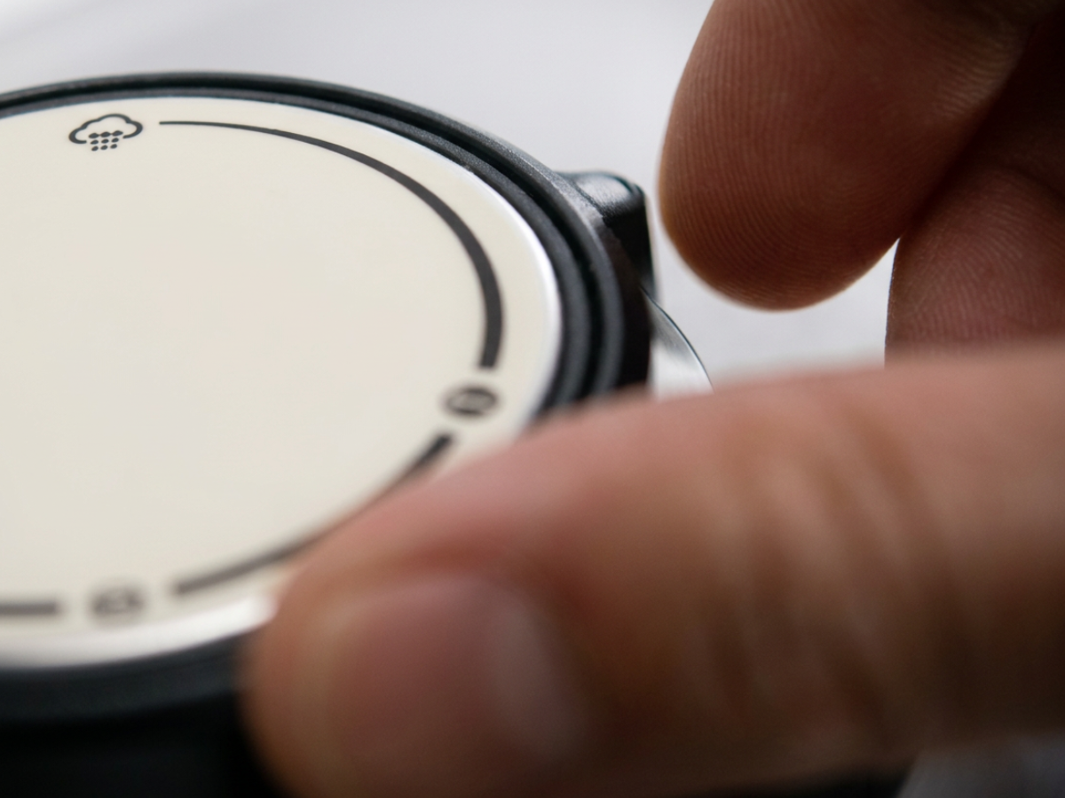 Eine Nahaufnahme der Hand einer Person, die den Rand eines Fissler-Schnellkochtopfdeckels hält; darauf ist ein rundes, helles Gesicht mit minimalen Markierungen und einem kleinen Wolkensymbol oben zu sehen, was das Bekenntnis der Marke zu präziser Technik und zeitloser deutscher Qualität widerspiegelt.