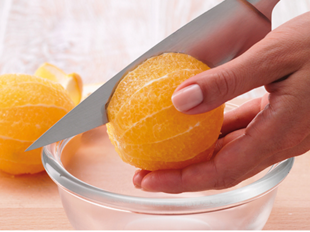 Eine Person schneidet mit einem hochwertigen Fissler-Messer eine geschälte Orange über einer Glasschale präzise ab, eine weitere Orange liegt daneben.