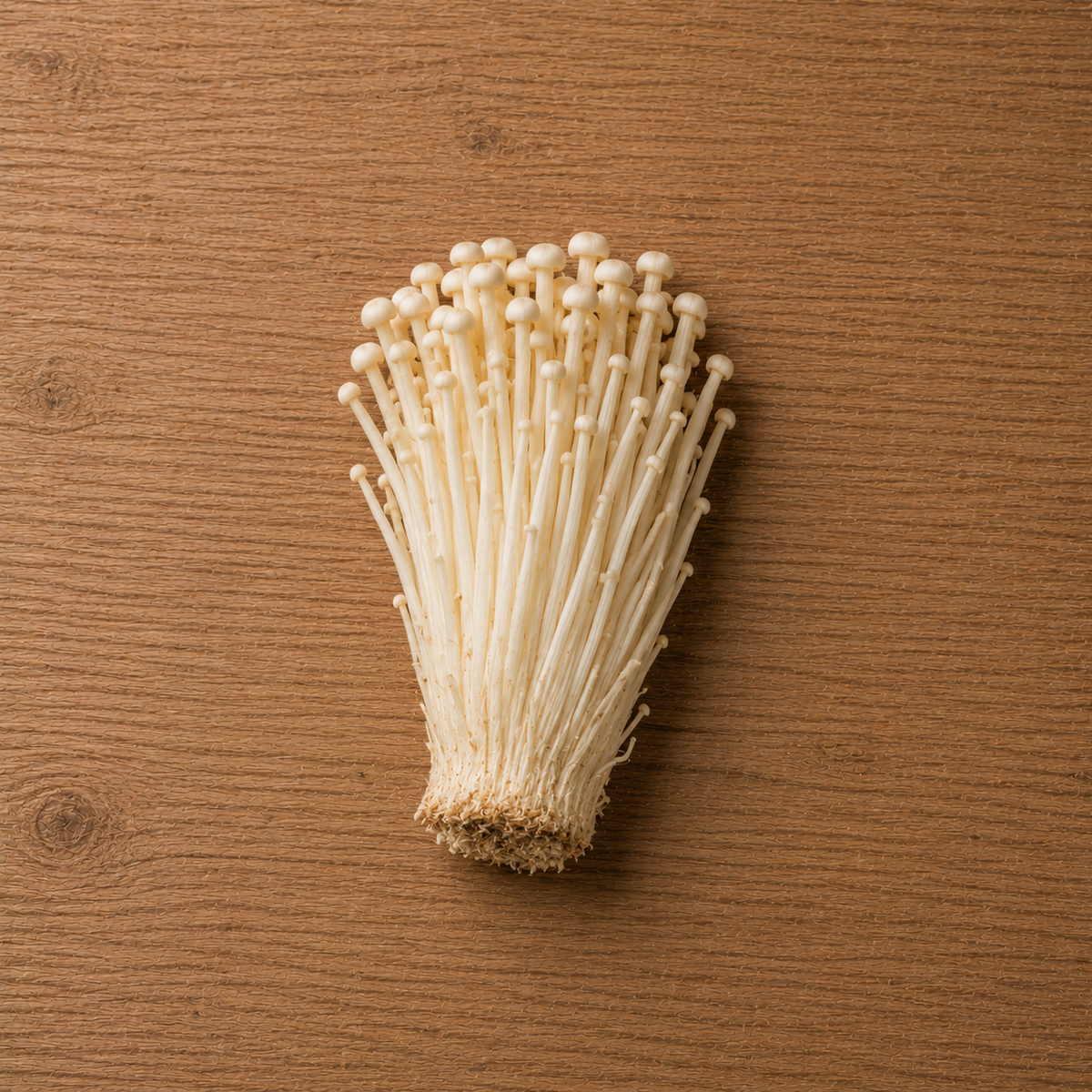 Enoki-Pilze mit langen, schlanken weißen Stielen und zierlichen Hüten, auf einer Holzunterlage angeordnet und bereit für die Zubereitung in Fisslers präzise gefertigten Kochgeschirren.